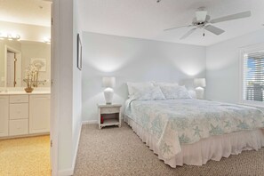 Une chambre à coucher avec un lit, des tables de chevet, un ventilateur de plafond et une fenêtre avec des stores.