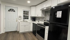 A modern kitchen with white cabinets, a black refrigerator, and a wooden floor. - Lakeside Hideaway (Lake Ronkonkoma)