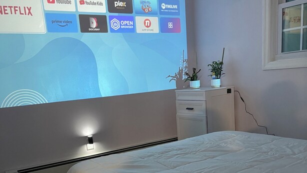 A bedroom with a bed, a dresser, a radiator, and a wall-mounted projector displaying various streaming services. - Lakeside Hideaway (Lake Ronkonkoma)