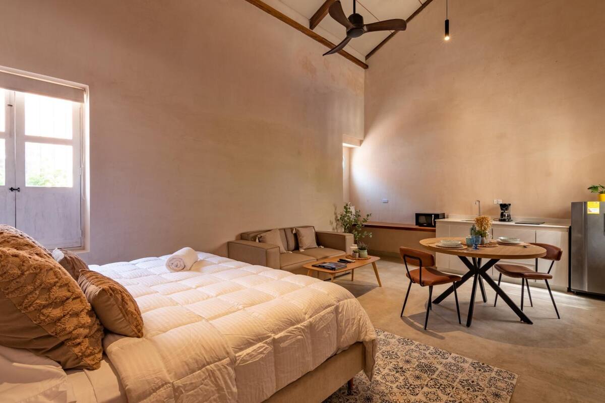 Un dormitorio moderno con una cama grande, un sofá, una mesa de comedor y una zona de cocina.