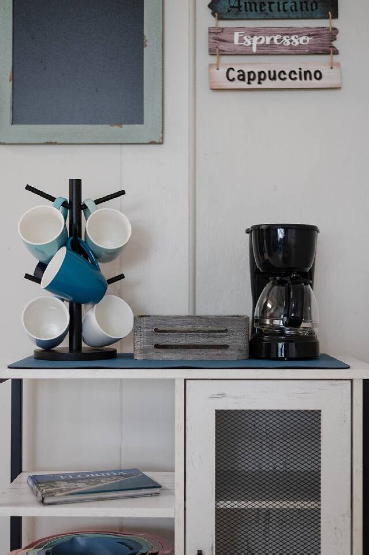 Una estación de café con una cafetera, un soporte para tazas y un cartel que indica los tipos de café.
