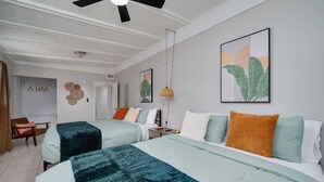 A hotel room with two beds, a ceiling fan, a wall-mounted artwork, and a door leading to another room.