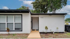 A modern single-story house with a beige exterior, a number '502' on the wall, and a small front yard with a few plants.