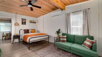 A cozy bedroom with a bed, a green sofa, a ceiling fan, and a window with curtains.