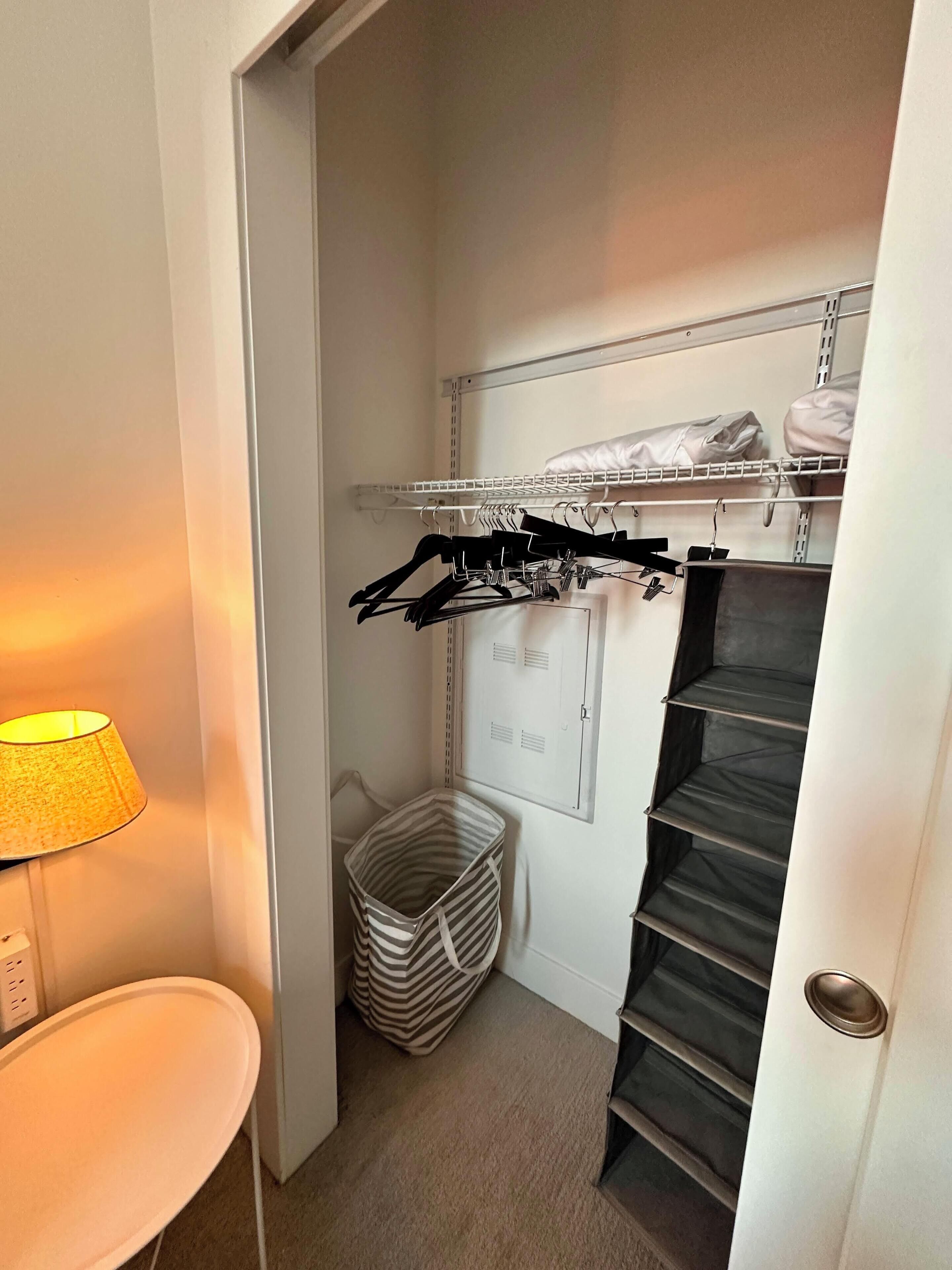 A compact room with a built-in closet, a small table with a lamp, and a striped laundry basket.