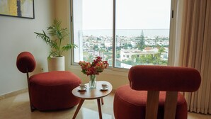 A modern living room with two red armchairs, a small table with a vase of flowers, and a large window offering a city view. - Luxury 3 Suites - Av Annakhil - Panoramic View (Rabat)