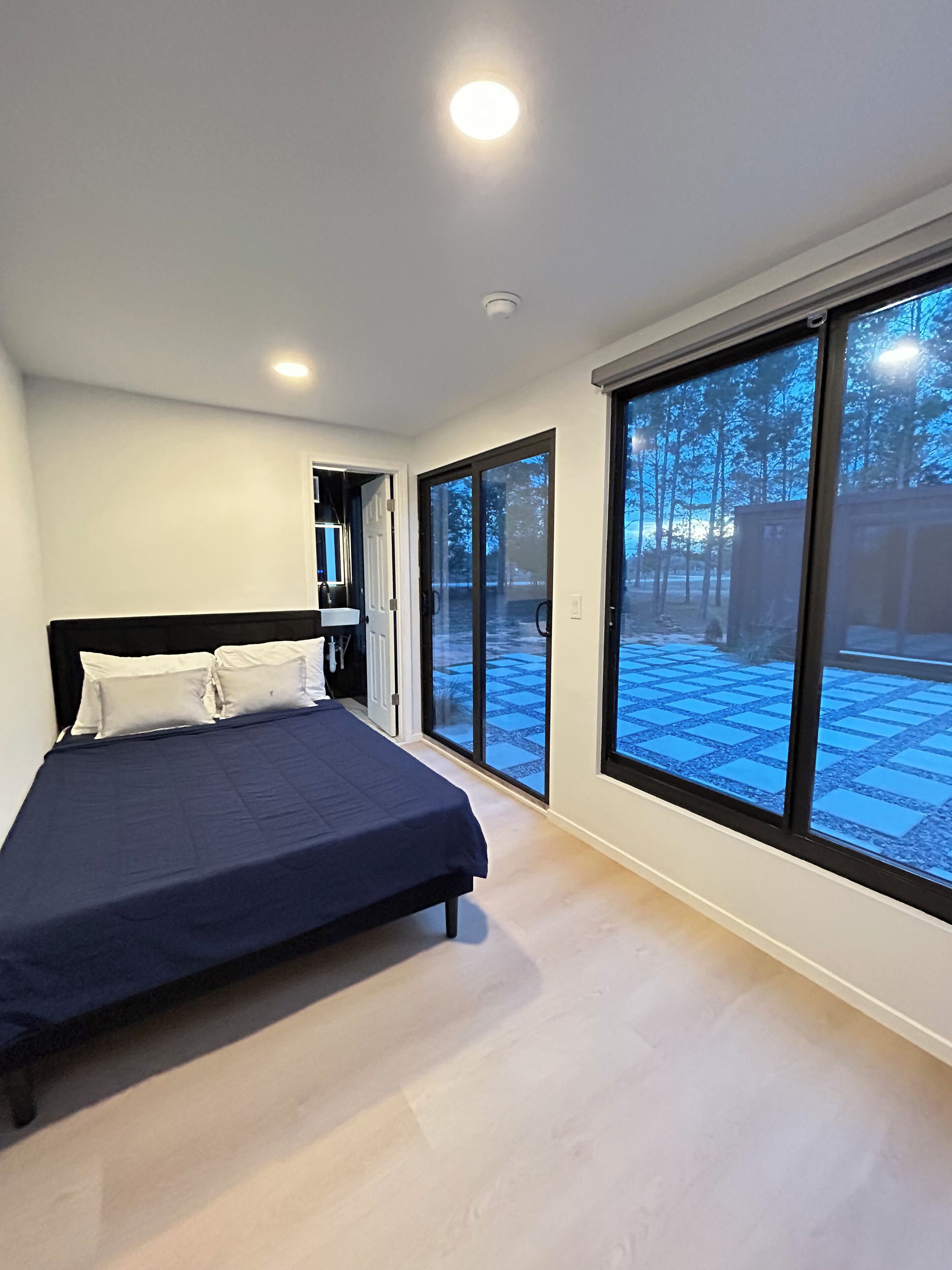 A bedroom with a bed, a large window, and a door leading outside.