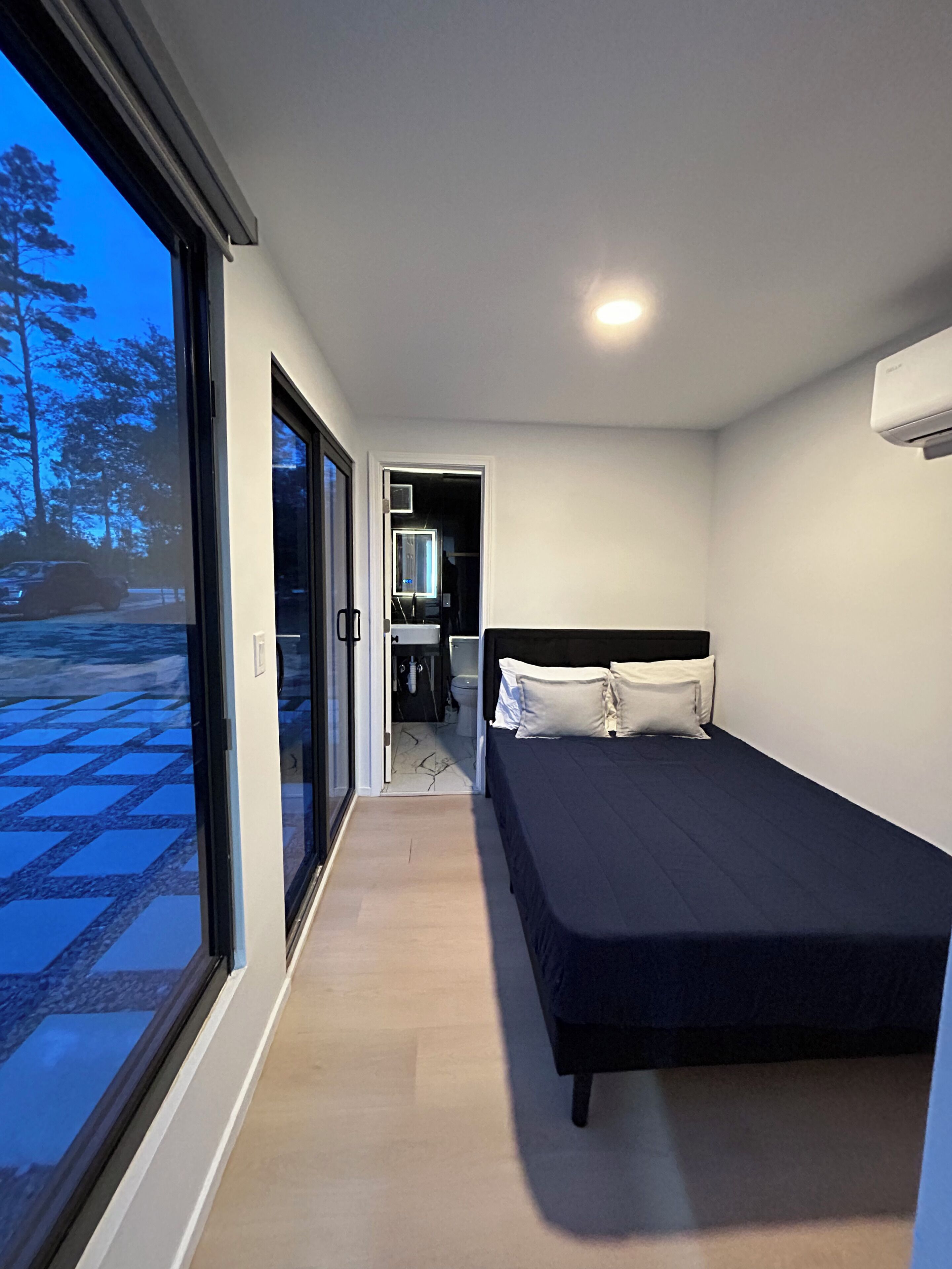 A modern bedroom with a large window, a bed, and a small bathroom.