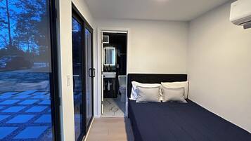 A modern bedroom with a large window, a bed, and a small bathroom.