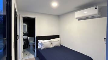 A bedroom with a bed, a wall-mounted air conditioner, and a bathroom visible through an open door.
