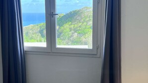 Et værelse med et vindue der udover et bjerglandskab og havet.