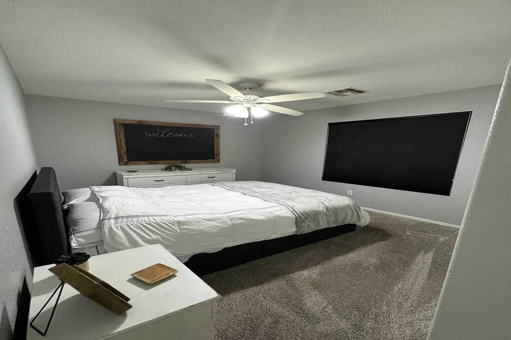 A bedroom with a bed, a desk, a television, a ceiling fan, a blackboard, and a window.