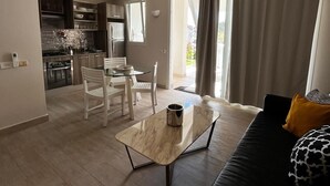 A modern living room with a black sofa, a marble coffee table, and a dining area with white chairs. - Sunset Paradise Tracadero Apartment: Sea pools access Private Garden WorkSpace (Dominicus)