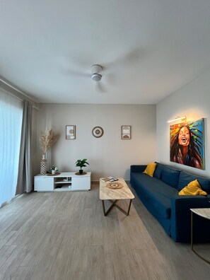Un salon moderne avec un canapé, une table basse, un meuble TV blanc et un ventilateur de plafond.