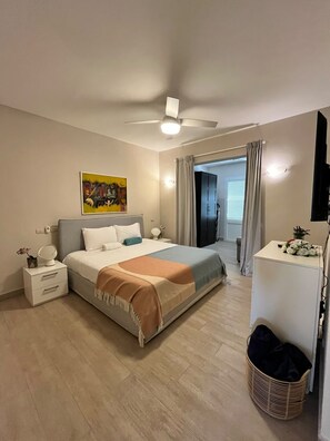 Ein Schlafzimmer mit Bett, Nachttischen, Deckenventilator, einem Gemälde, einem Kleiderschrank, einem Schreibtisch und einem Korb.
