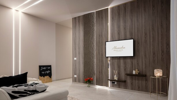 A modern living room with a white sofa, a flat-screen TV mounted on a wooden wall, a small table with decorative items, and a vase with red flowers. - AlexandraDesignSuite (Carpi)