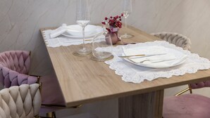 A dining table set with white plates, cutlery, and clear glasses, accompanied by a vase of flowers and a lace table runner. - AlexandraDesignSuite (Carpi)
