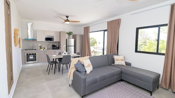 Ein modernes Wohnzimmer mit grauem Sofa, Esstisch und Küchenbereich.