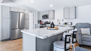 A modern kitchen with a central island, stainless steel appliances, and a grey sofa in the living area. - 4 BDR 2 mins from the River- Sleeps 12 (Bullhead City)