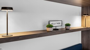 Habitació moderna amb una pràdua de fusta, dues plantes en test, un cartell que diu “HELLO THERE” i dues làmpades de peu.