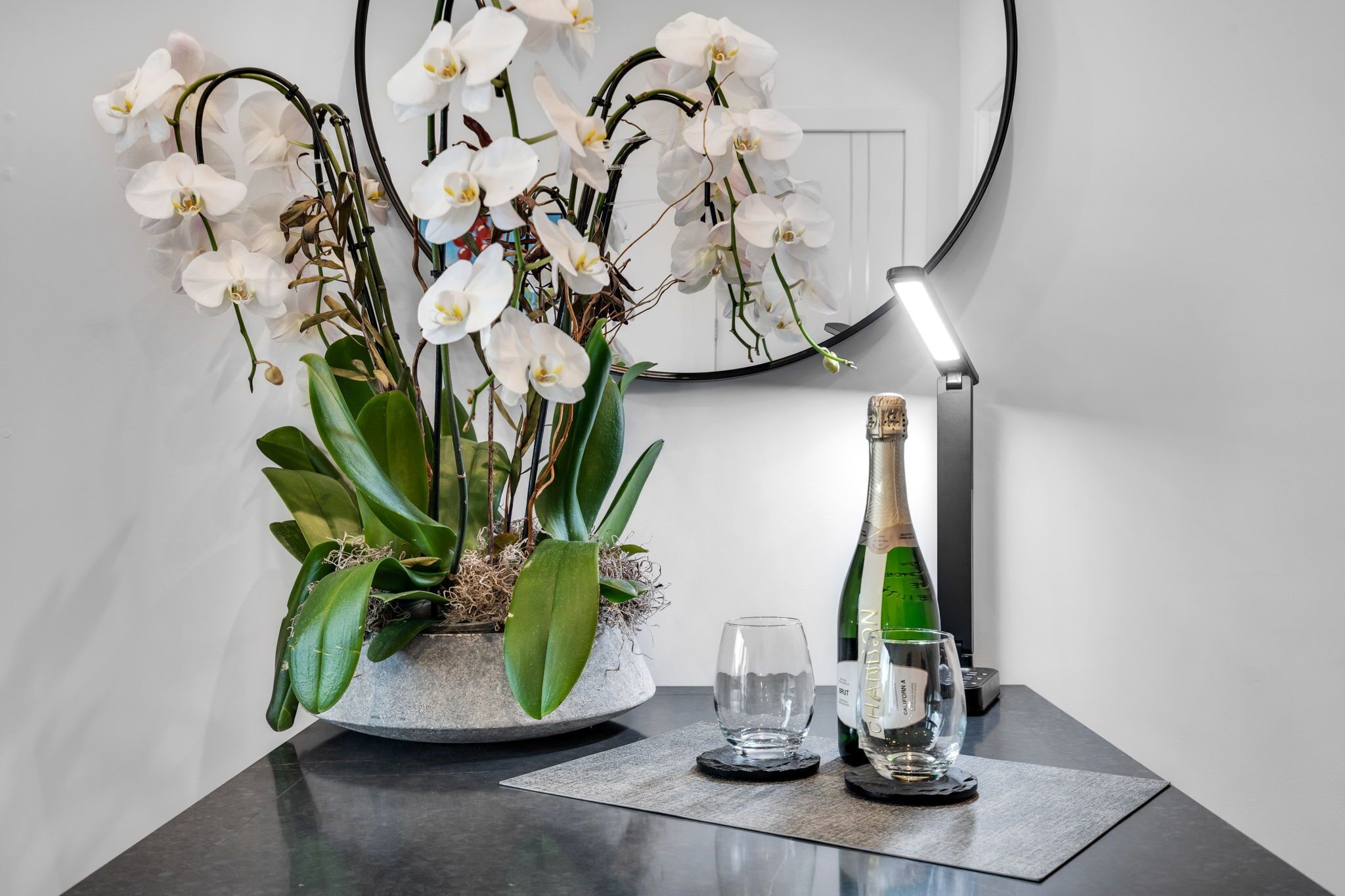 Une orchidée en pot, posée sur une table, avec une bouteille et deux verres.