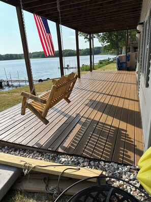 A wooden deck with a swing chair, a dock, and a view of a lake.
