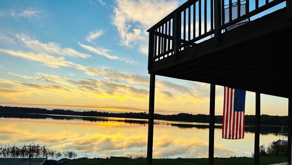 Een uitzicht op het water met een terras, een Amerikaanse vlag en een rustig meer dat de lucht weerspiegelt.