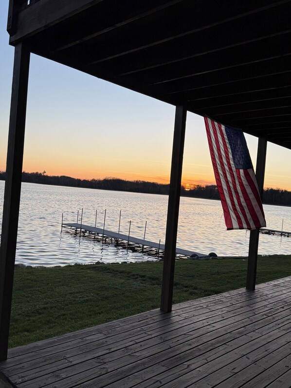 A wooden deck with an American flag, overlooking a calm lake with dock structures.