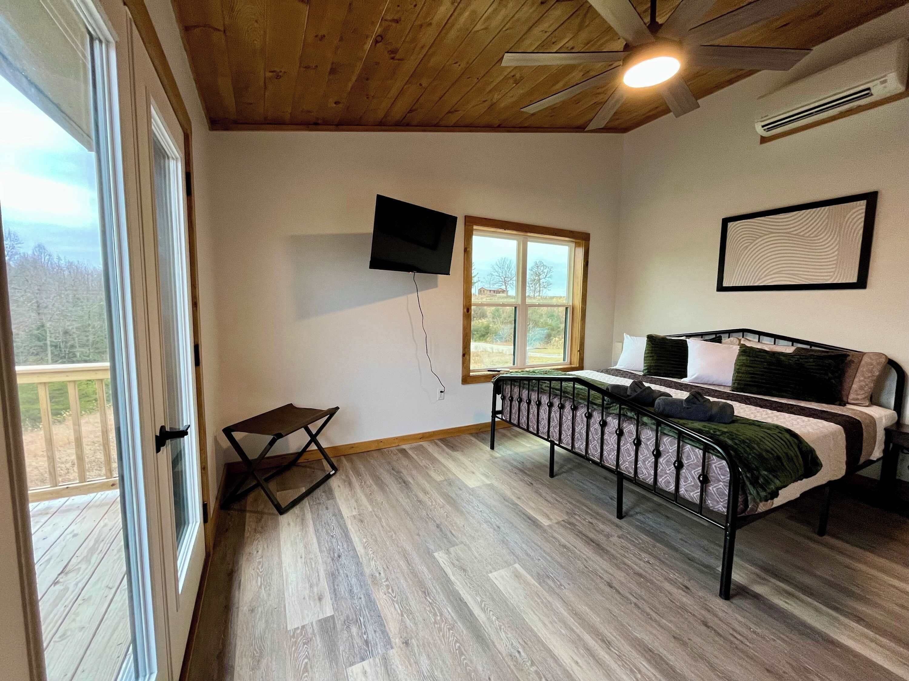 Een slaapkamer met een bed, een aan de muur bevestigde televisie, een raam en een plafondventilator.