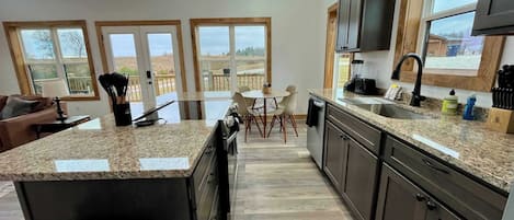Una cocina moderna con encimeras de granito, armarios oscuros y un amplio ventanal con vistas a una terraza.