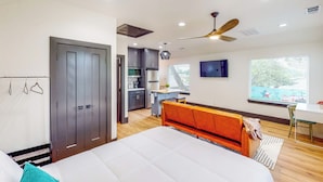 A bedroom with a bed, a desk, a chair, a wardrobe, and a kitchenette.