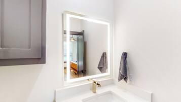 A bathroom with a white sink, a mirror with a lighted frame, and a towel hanging on the wall.