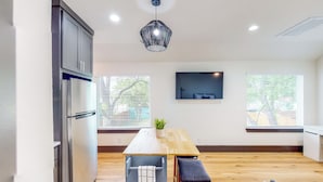 A modern kitchen with a built-in refrigerator, wooden dining table, and a hanging pendant light.