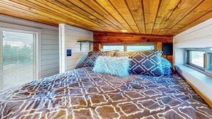 Ein Schlafzimmer mit Holzbalkendecke, einem gemusterten Bettüberwurf und einem Fenster mit Jalousien.