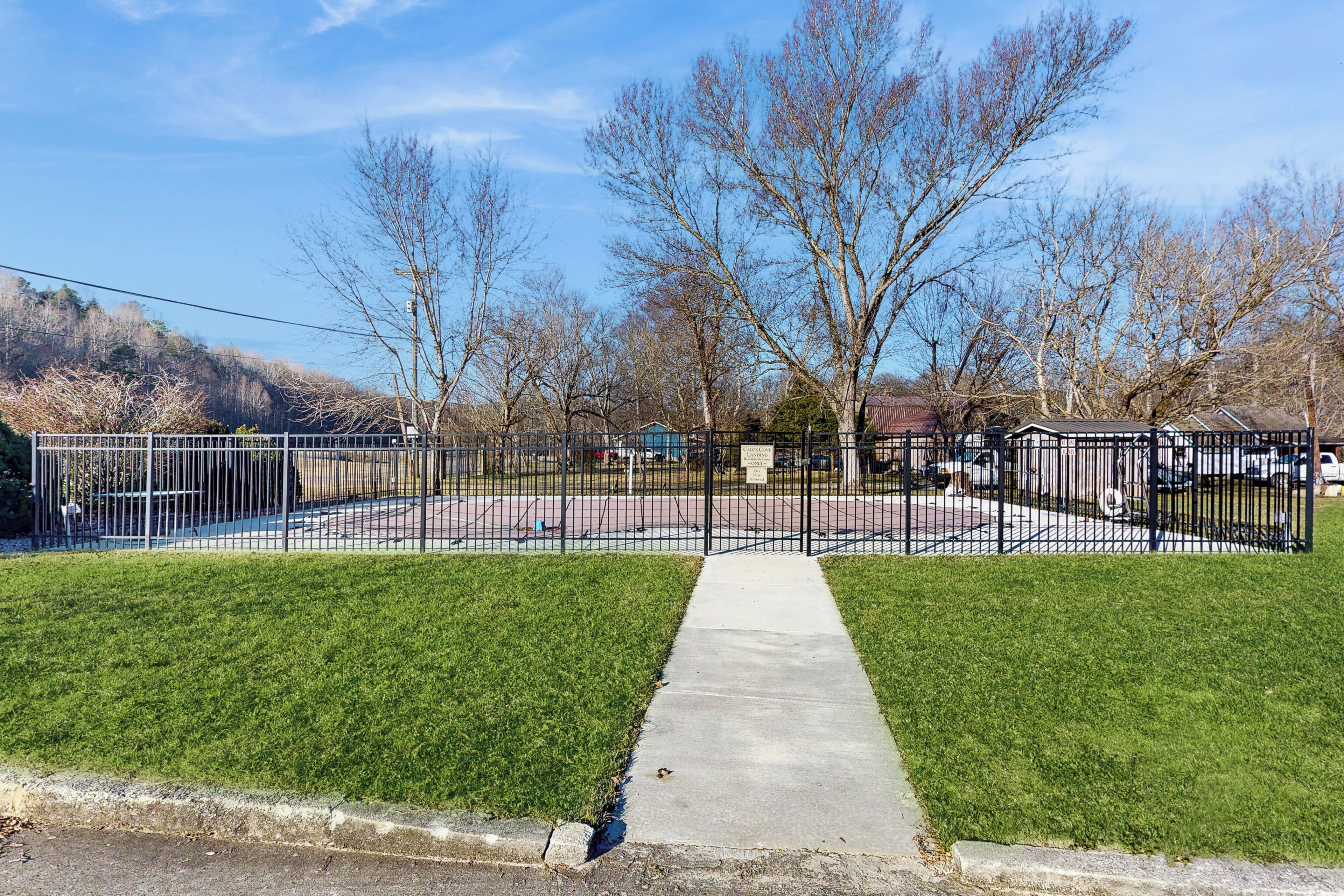 A fenced outdoor area with a concrete pathway, trees, and a building in the background.