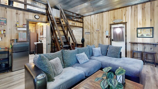 A cozy cabin-style room with a large L-shaped sectional sofa, a wooden ceiling, and a ladder leading to an upper level. - Close to Reelfoot Lake! Dog-Friendly Retreat (Tiptonville)