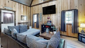 A wooden cabin interior with a sofa, a coffee table, and a TV mounted on the wall. - Close to Reelfoot Lake! Dog-Friendly Retreat (Tiptonville)