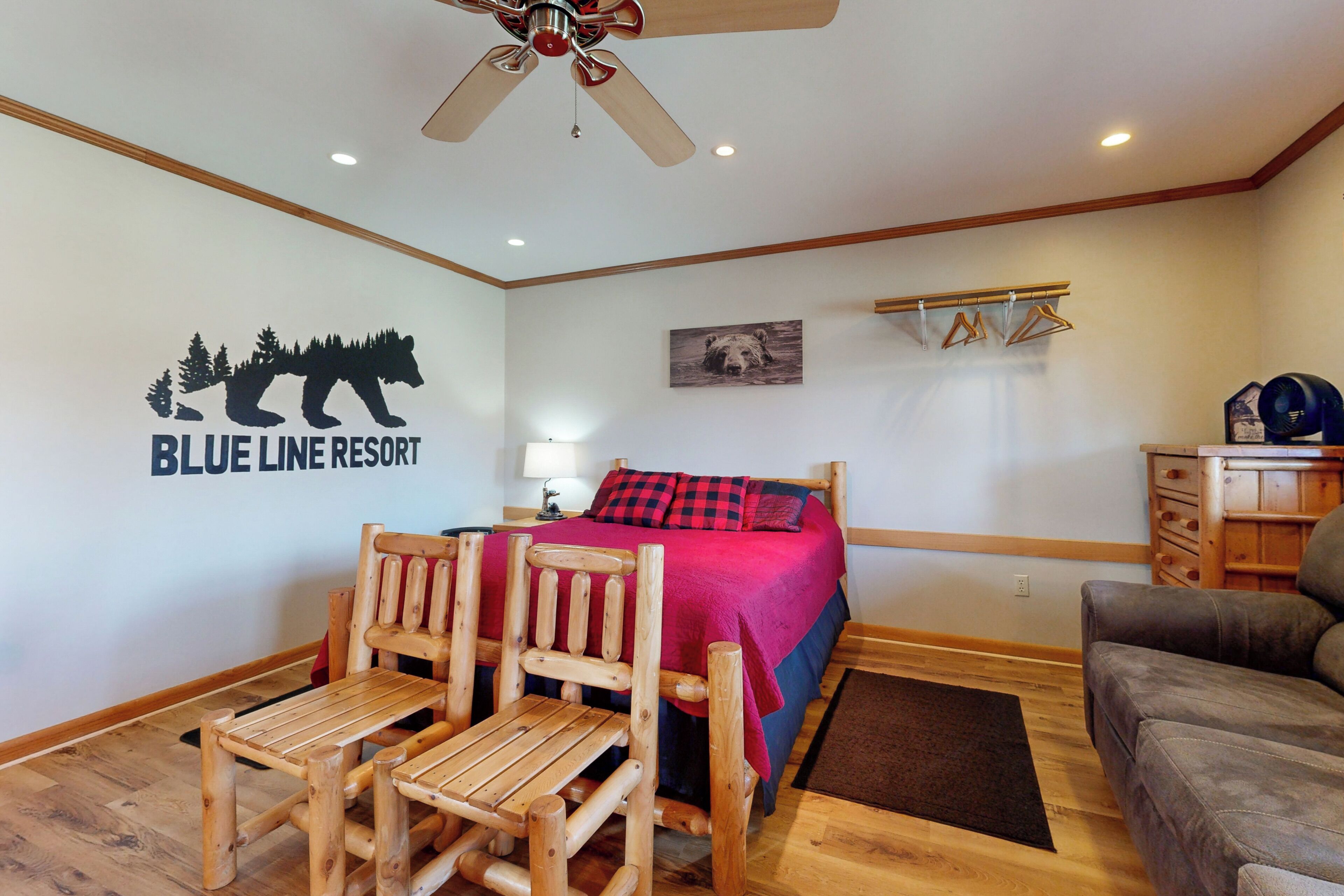 Habitació amb un llit, una cadira de fusta, un sofà, un ventilador de sostre i una paret amb el logotip de 'Blue Line Resort'.
