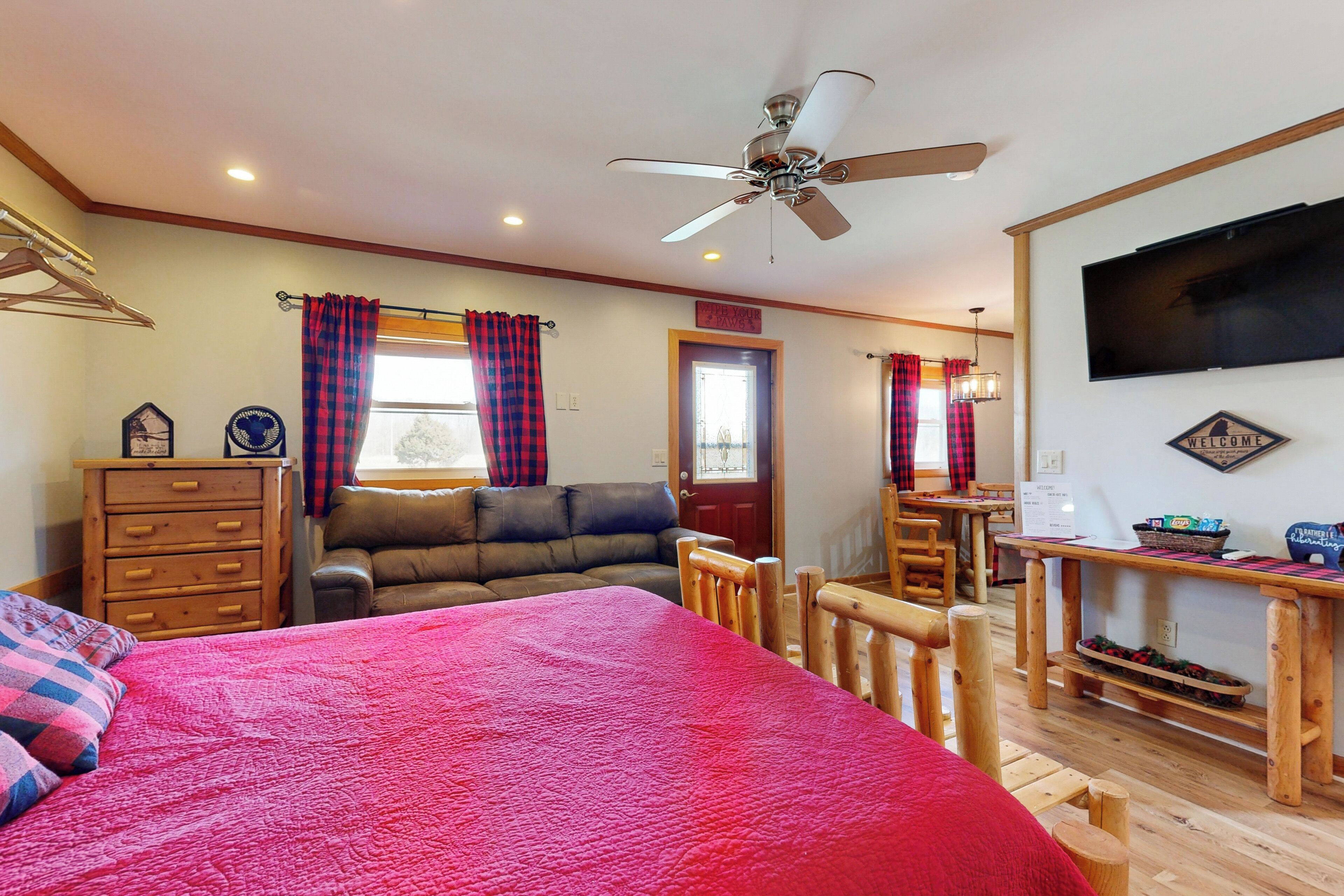A cozy room with a bed, a wooden dresser, a sofa, a dining table, and a ceiling fan.