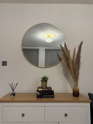 A room with a round mirror, a wooden dresser, a potted plant, and a vase with dried plants. - Cosy 2 Bedroom Flat in the Heart of Greenwich (London)