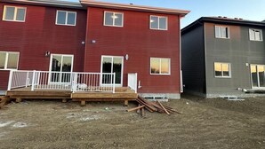A two-story building with a red exterior and a grey exterior. There is a wooden deck in front of the building. - Luxury Duplex in Spruce Grove (Spruce Grove)