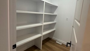 A walk-in closet with white shelving units and a wooden floor. - Luxury Duplex in Spruce Grove (Spruce Grove)