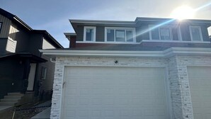 A two-story house with a garage, a stone facade, and a clear sky. - Luxury Duplex in Spruce Grove (Spruce Grove)