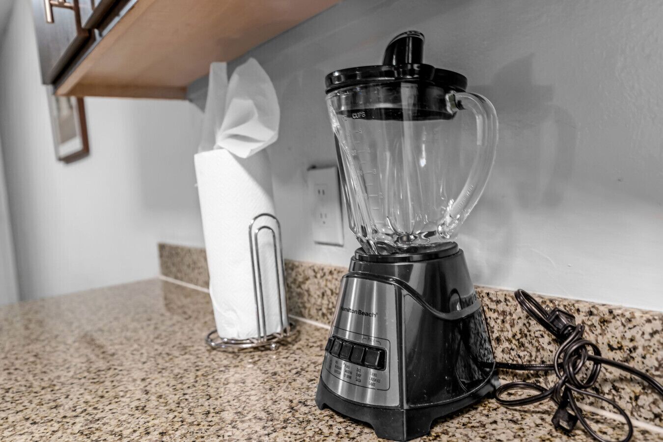 A kitchen with a blender on the counter, a paper towel dispenser, and a granite countertop.