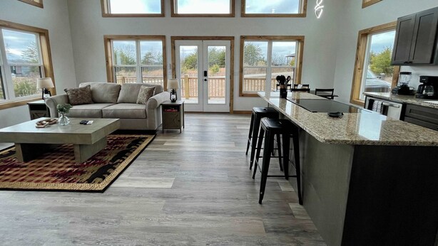 A spacious living area with a sofa, coffee table, and a kitchen with a bar. Large windows provide ample natural light. - Spruce Arch | King Bed; Fireplace; Pets Welcome! (Wolfe County)