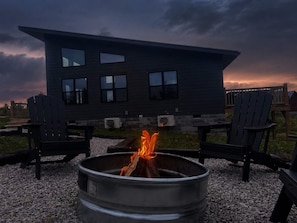Una casa moderna con un brasero al frente y dos sillas Adirondack.