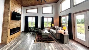 A spacious living room with a wooden ceiling, large windows, a fireplace, and a television mounted on the wall. - Spruce Arch | King Bed; Fireplace; Pets Welcome! (Wolfe County)
