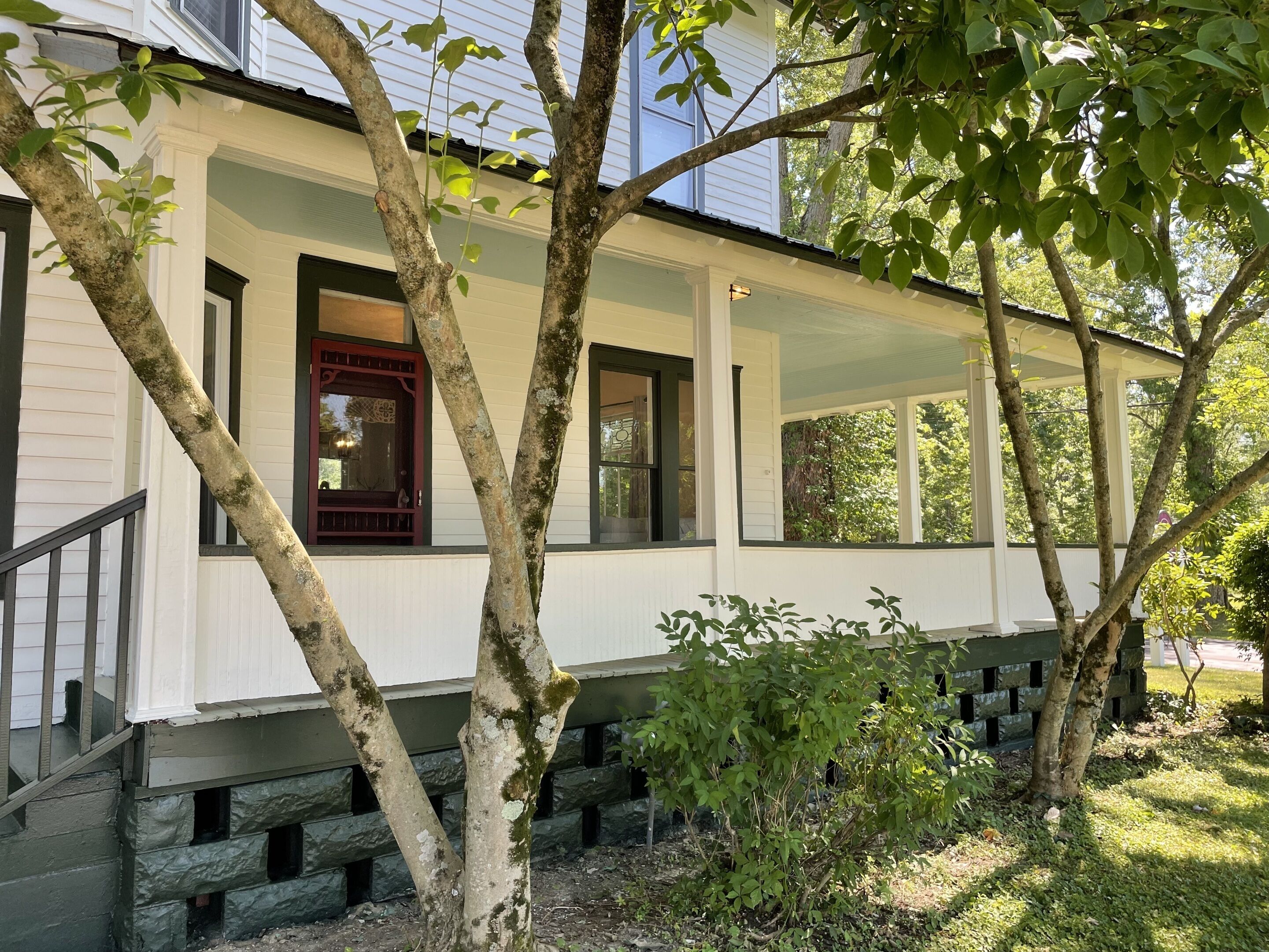 A white building with a porch, a red door, and a stone staircase.
