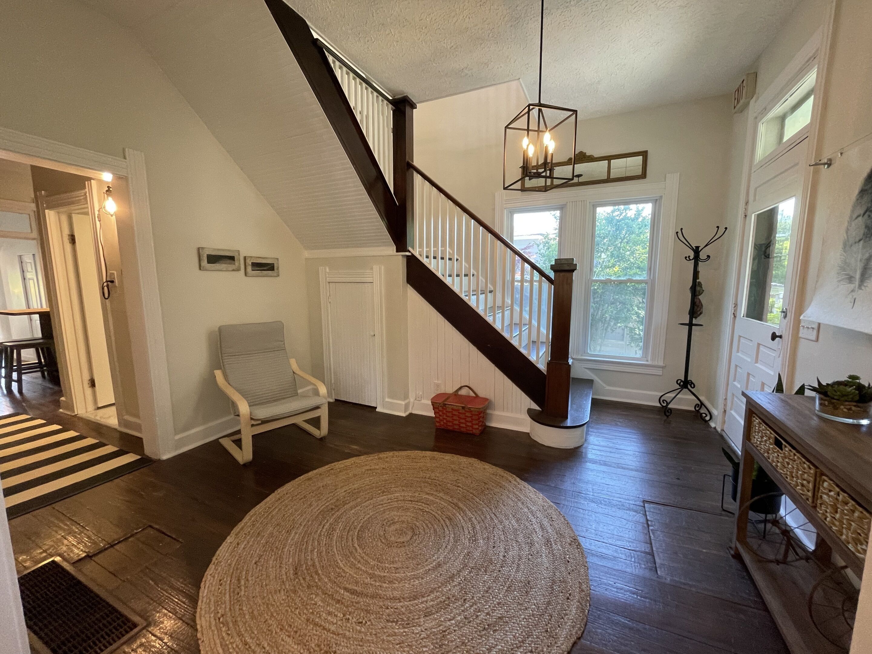 A spacious living room with a wooden staircase, a round woven rug, and a dining area with a striped rug.