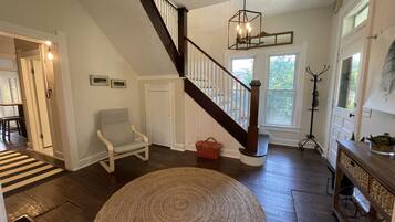 A spacious living room with a wooden staircase, a round woven rug, and a dining area with a striped rug.